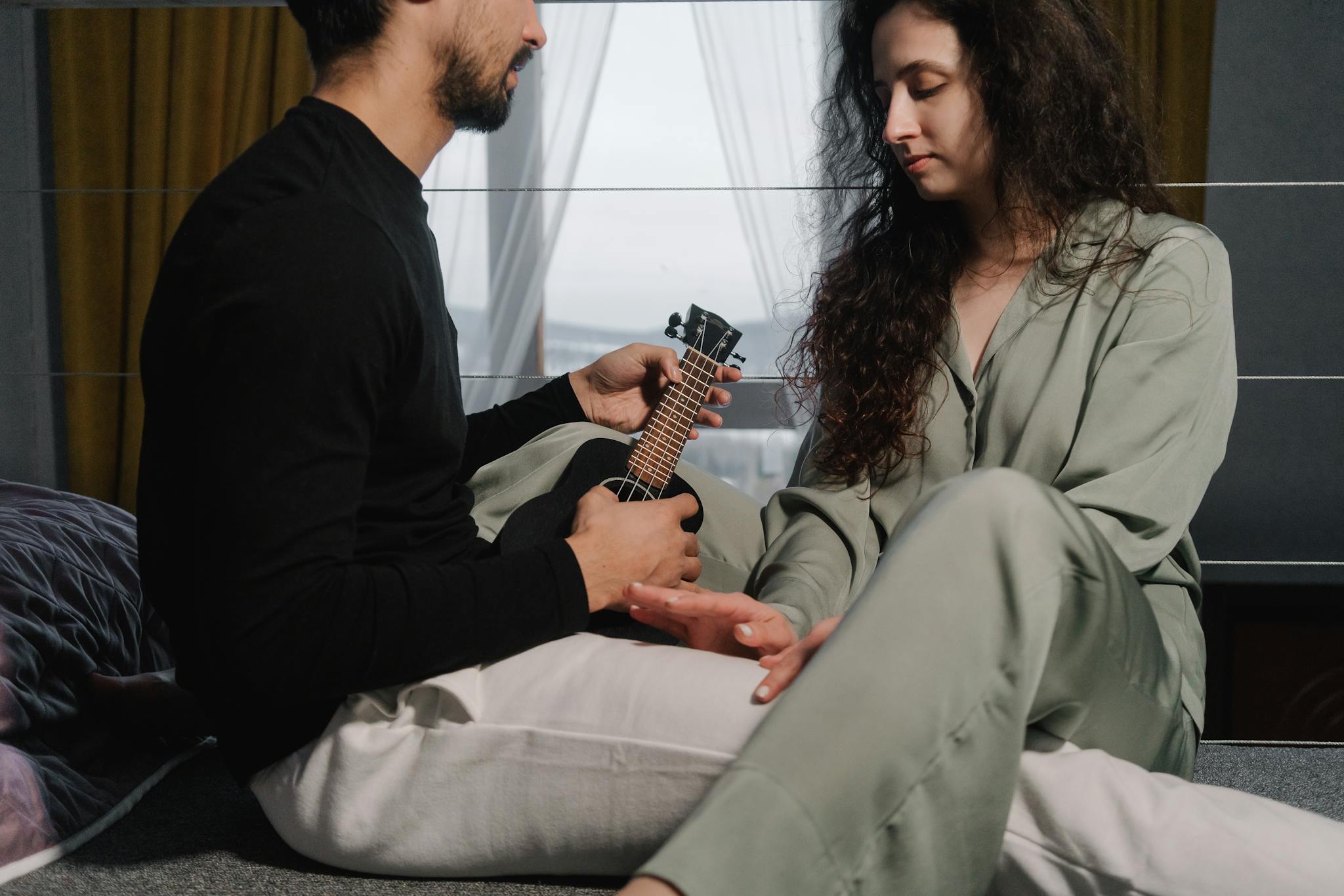A couple enjoying a quiet moment together, playing a ukulele indoors, showcasing connection and music.