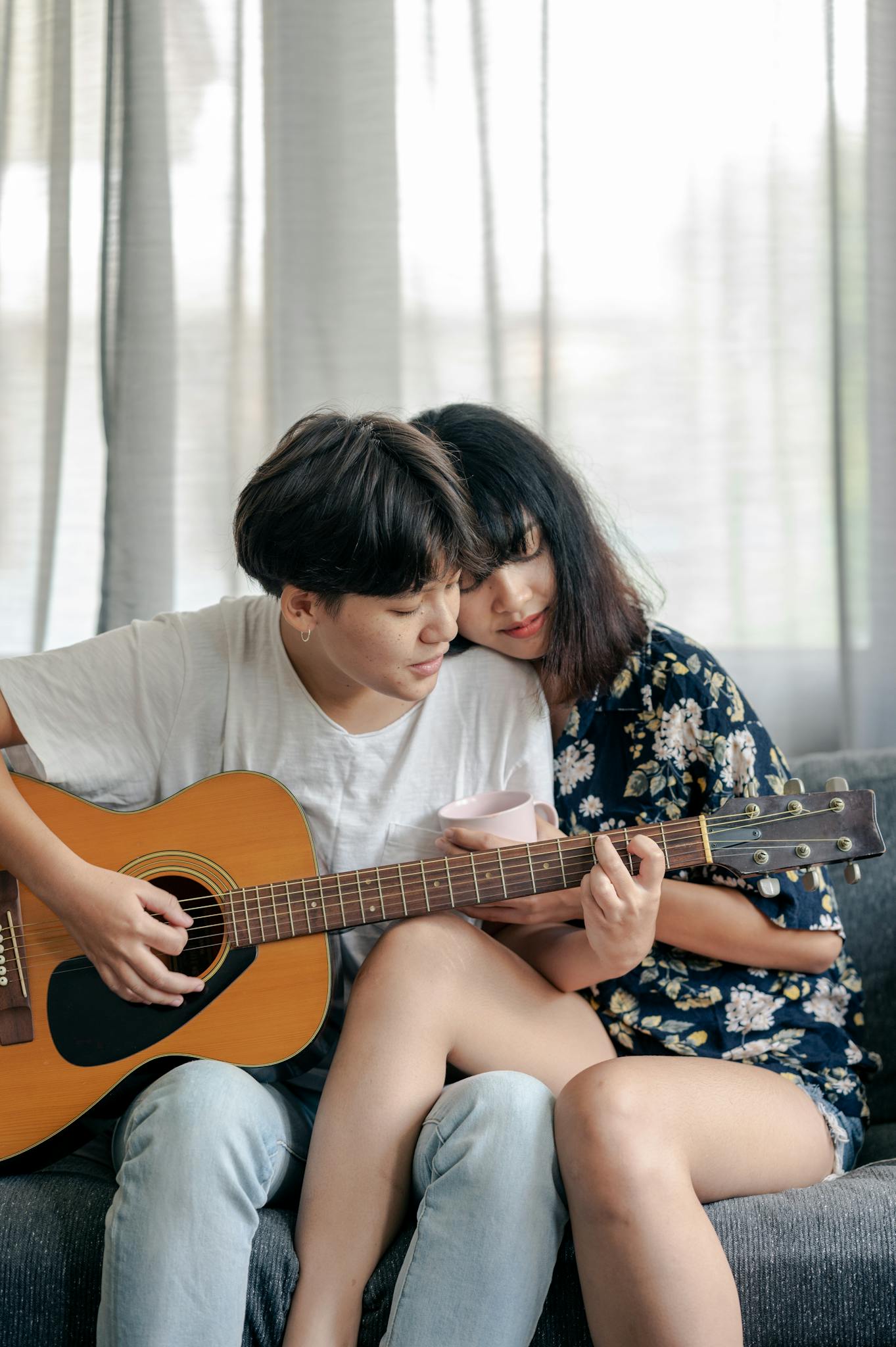 A couple shares an affectionate moment playing guitar together indoors.